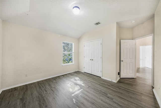 unfurnished bedroom with vaulted ceiling, dark hardwood / wood-style flooring, a textured ceiling, and a closet