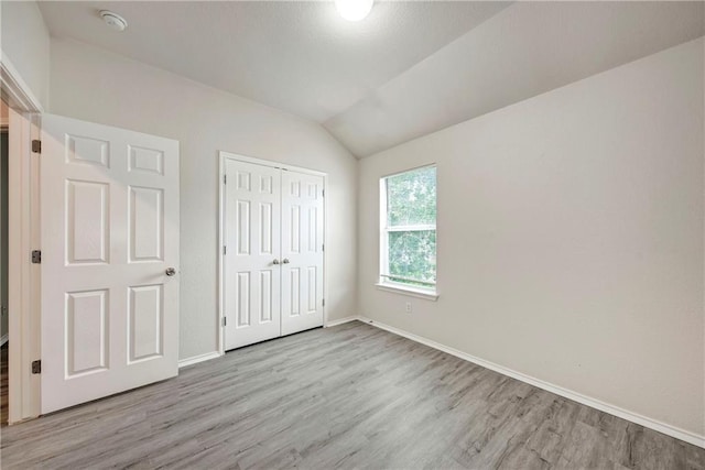 unfurnished bedroom with light wood-type flooring, lofted ceiling, and a closet