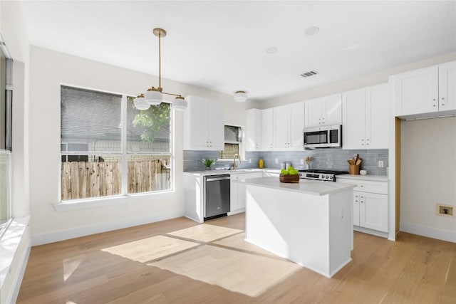 kitchen featuring stainless steel appliances, a kitchen island, pendant lighting, light hardwood / wood-style flooring, and white cabinetry