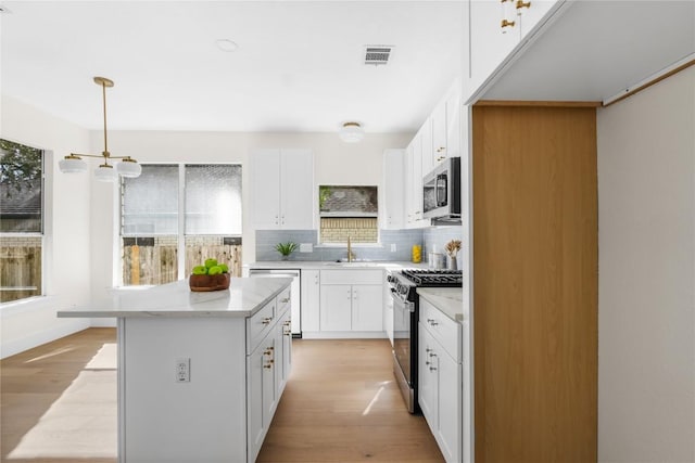 kitchen featuring hanging light fixtures, light hardwood / wood-style flooring, backsplash, white cabinets, and appliances with stainless steel finishes