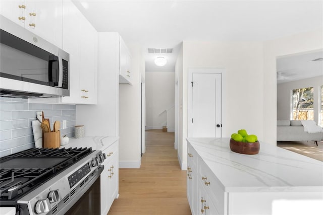 kitchen with backsplash, light stone countertops, light wood-type flooring, appliances with stainless steel finishes, and white cabinetry