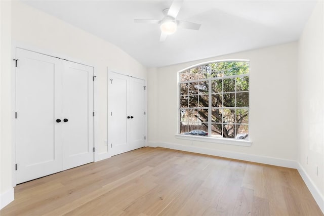 unfurnished bedroom with vaulted ceiling, two closets, light hardwood / wood-style flooring, and ceiling fan