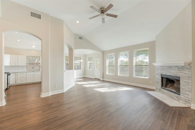 unfurnished living room featuring ceiling fan with notable chandelier, sink, high vaulted ceiling, dark hardwood / wood-style floors, and a stone fireplace