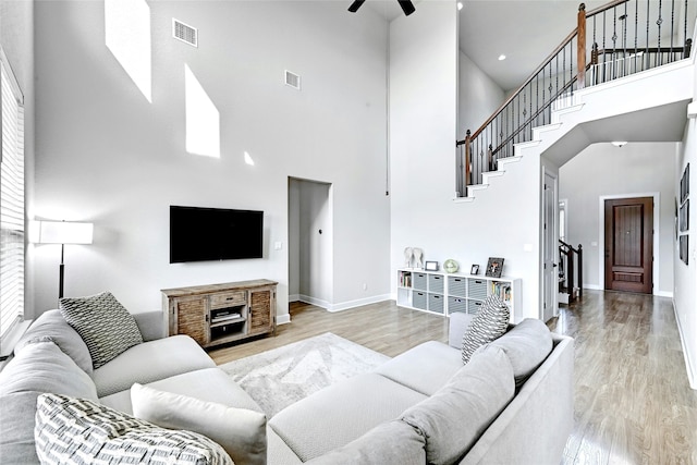 living room with a towering ceiling, ceiling fan, and light hardwood / wood-style flooring