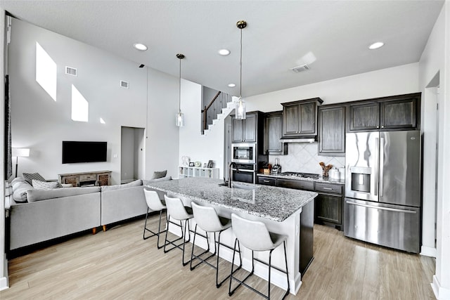 kitchen featuring a breakfast bar area, appliances with stainless steel finishes, an island with sink, light stone counters, and backsplash