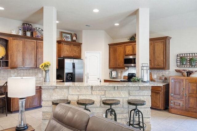 kitchen with light stone countertops, kitchen peninsula, tasteful backsplash, stainless steel appliances, and a breakfast bar area