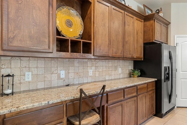 kitchen with backsplash, light stone counters, light tile patterned floors, and stainless steel refrigerator with ice dispenser