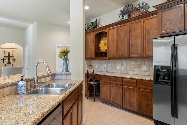 kitchen with appliances with stainless steel finishes, backsplash, light stone counters, sink, and light tile patterned floors