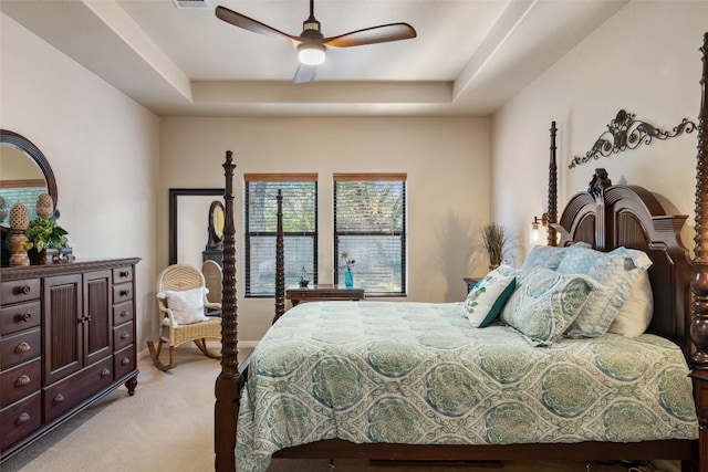 bedroom featuring light carpet, a tray ceiling, and ceiling fan