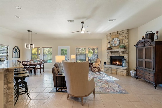 living room with a stone fireplace, ceiling fan, and light tile patterned flooring