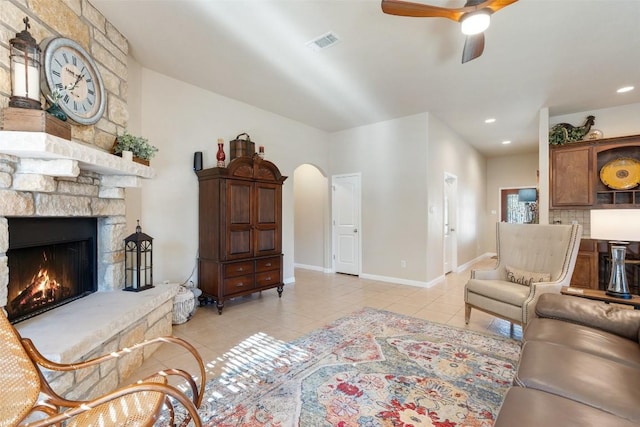 tiled living room featuring a stone fireplace and ceiling fan