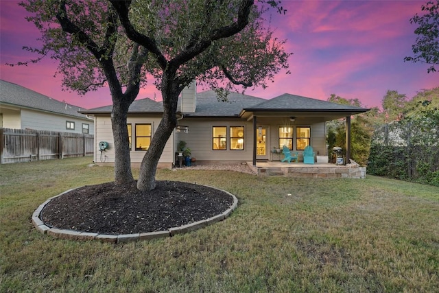 back house at dusk with a lawn and a patio