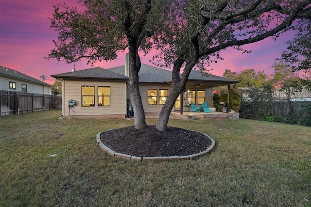 back house at dusk featuring a patio area and a lawn