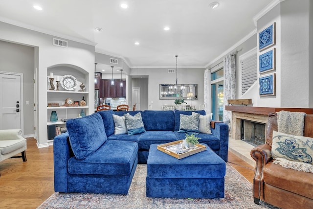 living room featuring built in features, light hardwood / wood-style floors, a notable chandelier, and ornamental molding