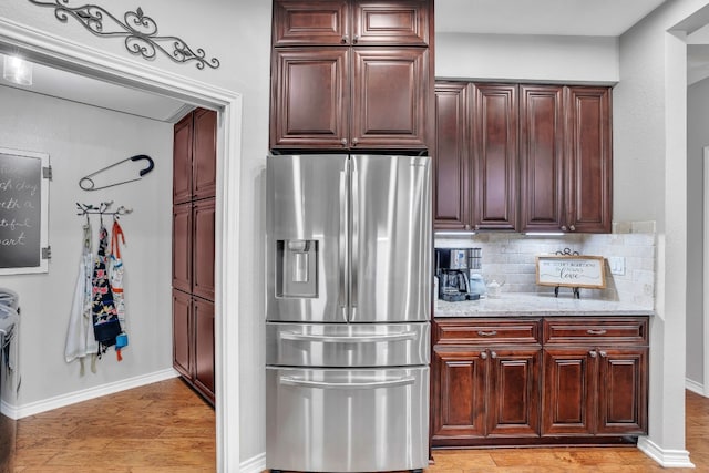 kitchen with light stone countertops, stainless steel fridge with ice dispenser, light wood-type flooring, and tasteful backsplash