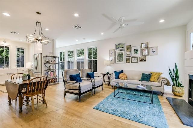 living room featuring light hardwood / wood-style flooring, ceiling fan with notable chandelier, and sink