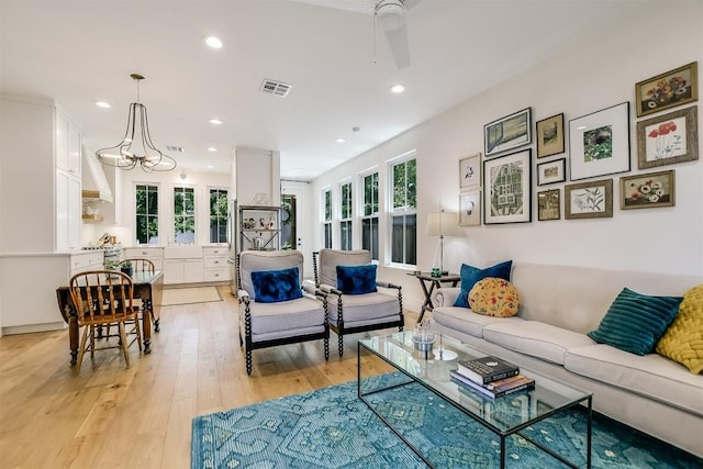 living room with ceiling fan with notable chandelier and light wood-type flooring