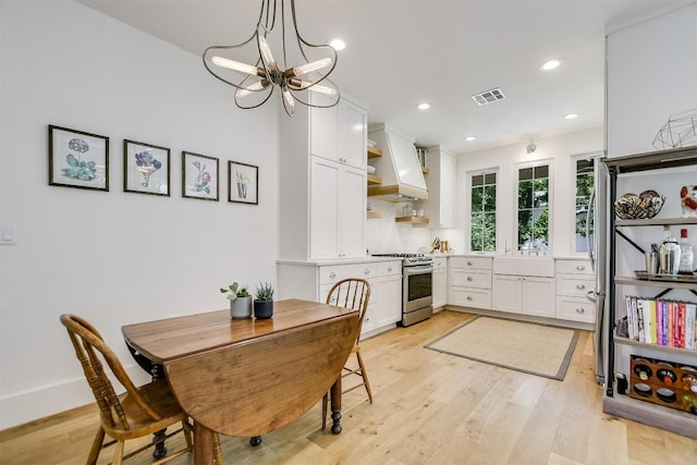 kitchen with stainless steel range, light hardwood / wood-style flooring, decorative light fixtures, white cabinets, and custom range hood