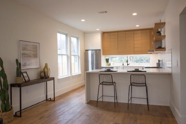 kitchen with stainless steel refrigerator, light hardwood / wood-style flooring, kitchen peninsula, a breakfast bar area, and decorative backsplash