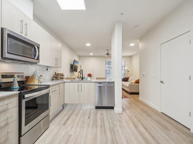 kitchen with appliances with stainless steel finishes, light wood-type flooring, ceiling fan, and sink