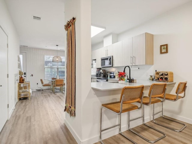 kitchen featuring a breakfast bar, hanging light fixtures, appliances with stainless steel finishes, light hardwood / wood-style floors, and kitchen peninsula