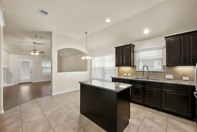 kitchen with sink, light stone counters, decorative light fixtures, vaulted ceiling, and a kitchen island