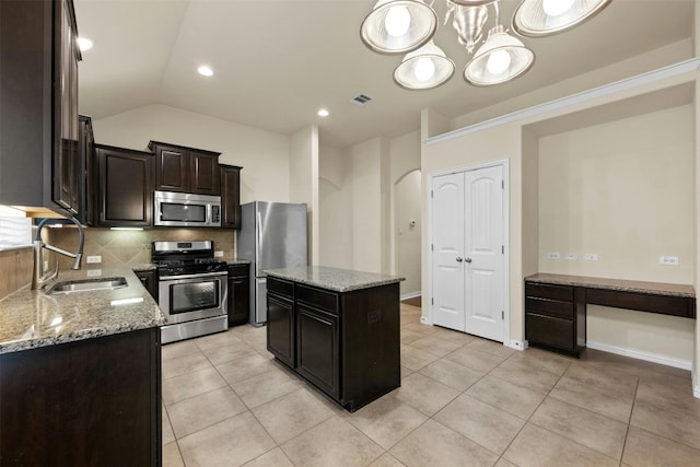 kitchen with appliances with stainless steel finishes, light stone counters, vaulted ceiling, sink, and a center island