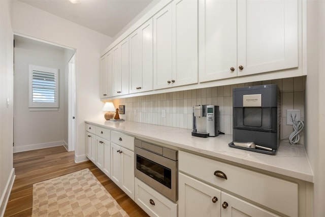 kitchen featuring backsplash, light stone counters, light hardwood / wood-style flooring, white cabinets, and stainless steel microwave