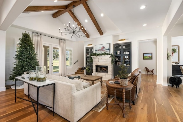 living room with beam ceiling, a stone fireplace, a notable chandelier, and hardwood / wood-style flooring