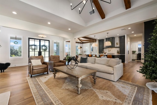 living room featuring a notable chandelier, lofted ceiling with beams, and light hardwood / wood-style flooring