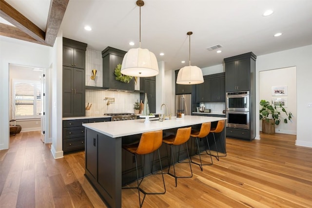 kitchen featuring stainless steel appliances, beamed ceiling, pendant lighting, decorative backsplash, and hardwood / wood-style flooring