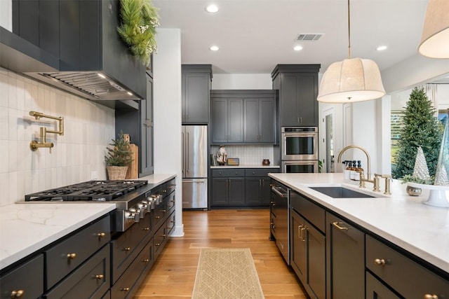 kitchen featuring sink, stainless steel appliances, wall chimney range hood, pendant lighting, and light hardwood / wood-style floors