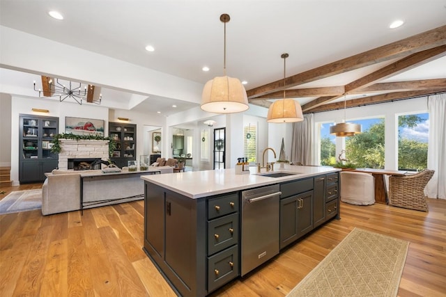 kitchen with pendant lighting, a kitchen island with sink, sink, stainless steel dishwasher, and light wood-type flooring