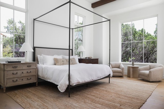 bedroom featuring beamed ceiling, multiple windows, and wood finished floors