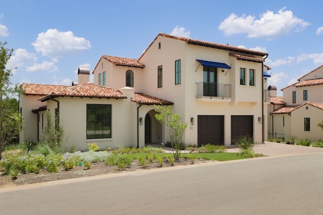 mediterranean / spanish home featuring a garage, a tiled roof, concrete driveway, and stucco siding