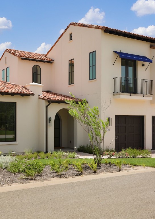 mediterranean / spanish house with a balcony, a tile roof, an attached garage, and stucco siding