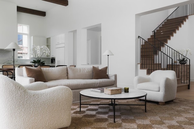 living area featuring stairway, a towering ceiling, wood finished floors, beamed ceiling, and baseboards