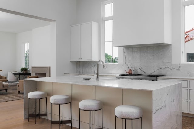 kitchen featuring light wood finished floors, range, light stone countertops, white cabinetry, and backsplash