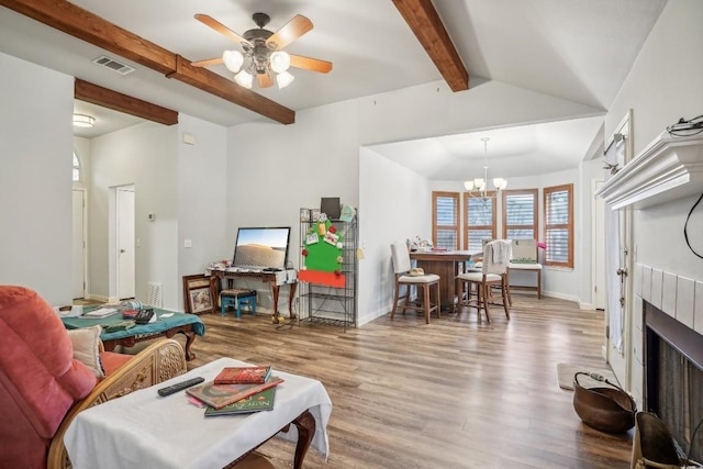 living room with a tiled fireplace, ceiling fan with notable chandelier, lofted ceiling with beams, and light hardwood / wood-style floors