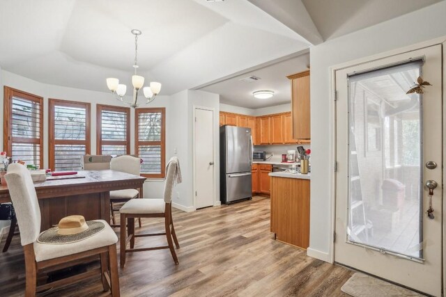 kitchen with an inviting chandelier, hanging light fixtures, stainless steel refrigerator, a raised ceiling, and light hardwood / wood-style floors