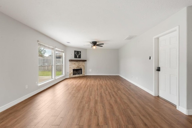 unfurnished living room with hardwood / wood-style flooring, ceiling fan, and a stone fireplace