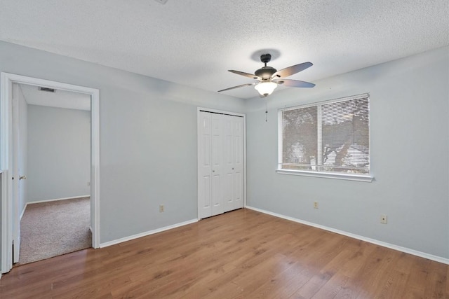 unfurnished bedroom featuring wood-type flooring, a textured ceiling, a closet, and ceiling fan