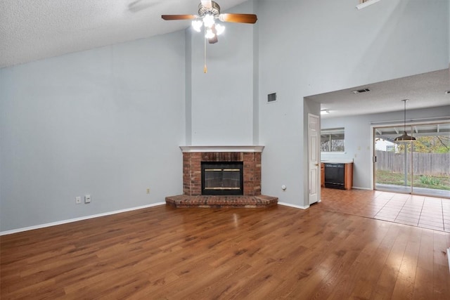 unfurnished living room with a fireplace, hardwood / wood-style floors, high vaulted ceiling, and a textured ceiling