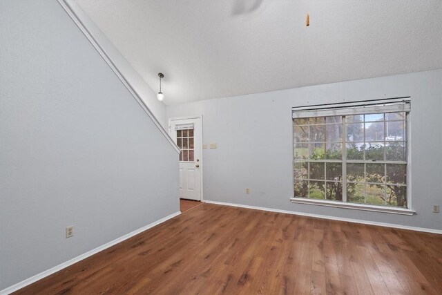 unfurnished room with a textured ceiling, vaulted ceiling, and hardwood / wood-style flooring