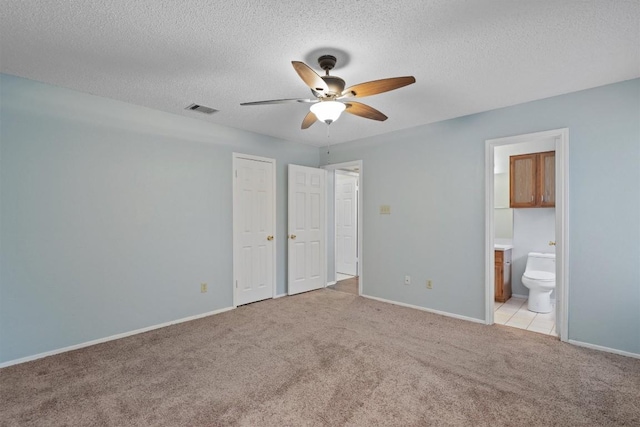 unfurnished bedroom featuring ensuite bathroom, ceiling fan, light colored carpet, and a textured ceiling