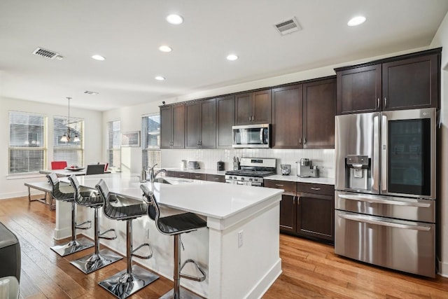 kitchen featuring stainless steel appliances, light hardwood / wood-style flooring, hanging light fixtures, and a kitchen island with sink