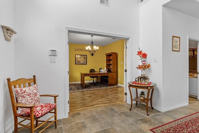 corridor with baseboards, wood finished floors, visible vents, and an inviting chandelier