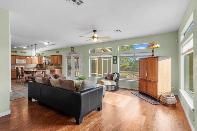 living room with visible vents, ceiling fan, light wood-style flooring, and baseboards