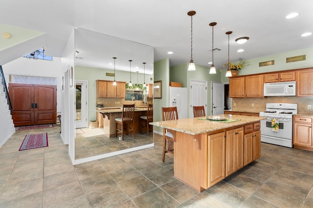 kitchen featuring light stone countertops, white appliances, a kitchen island, a kitchen breakfast bar, and decorative backsplash