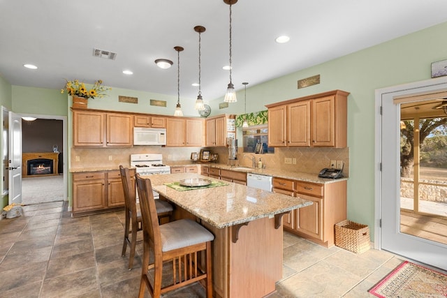 kitchen featuring a breakfast bar area, visible vents, a kitchen island, a warm lit fireplace, and white appliances